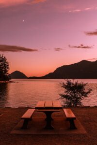 brown wooden table and bench near body of water during sunset